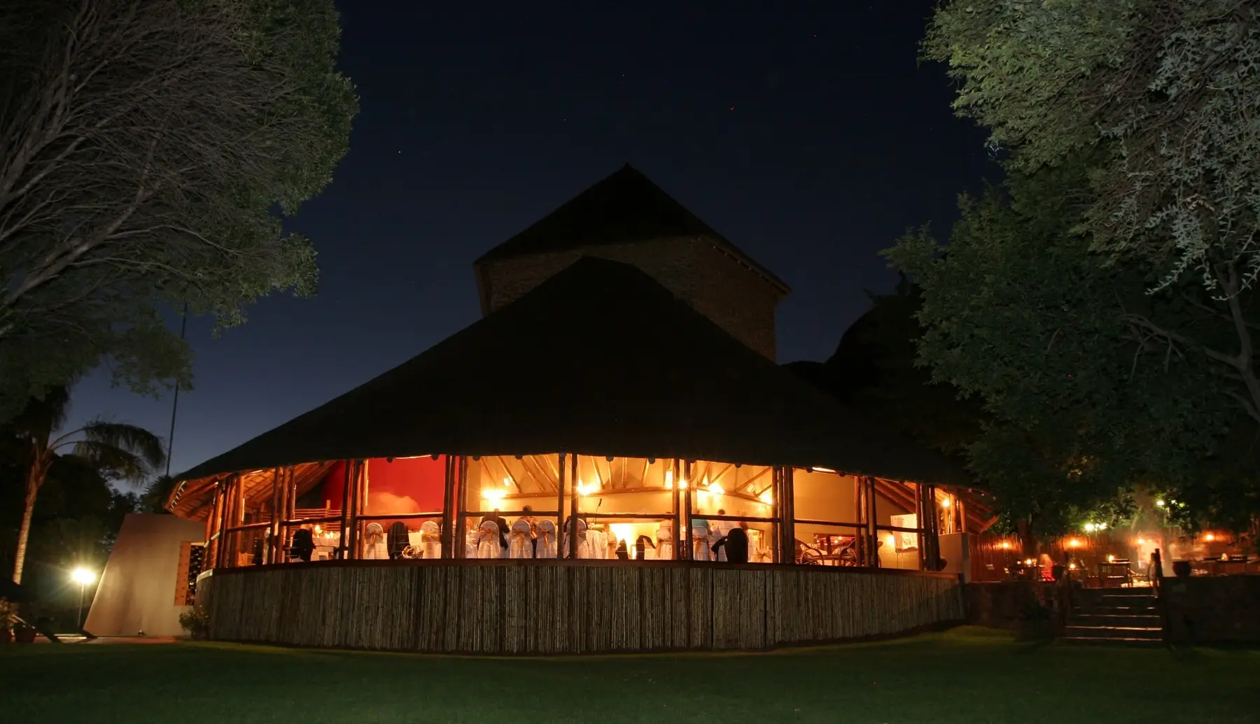 The lodge's thatched veranda lit up at night beside the boma